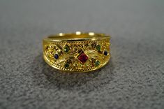 I am offering you this fabulous vintage  yellow gold tone wedding band stacker design ring. This piece is distinctive and stunning with the following features: It features 7 total combination round and square shaped oval cut bezel set emerald green, ruby and blue sapphire colored glass stones. These stones are set in a distinctive multi stone raised relief scrolled design setting. What a fantastic Etruscan style ring we have here. It is currently a size 8.  It measures app. 3/4 inch, by app. 1/2 Gold Ruby Ring With 17 Jewels For Wedding, Gold Ruby Ring With Intricate Design For Anniversary, Anniversary Gold Ruby Ring With Intricate Design, Gold Ruby Ring With Intricate Design For Wedding, Victorian Gold Rings For Marriage, Antique Gold Ring With Multi-stone, Antique Gold Multi-stone Ring, Gold Multi-stone Rings For Wedding, Gold Multi-stone Ruby Promise Ring