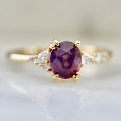 a close up view of a ring with an oval shaped ruby stone and diamond accents