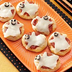 small pizzas with white icing and black eyes on an orange plate next to halloween decorations