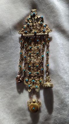 This very ornate chatelaine is fire gilded on brass. It is studded throughout with small Persian turquoise and is ornately hand chased and pierced. The chatelaine is 5 inches long (without the added drops), by 2 inches wide. It has later added fobs and a perfume with out the lid. The piece at some point was repaired with soft solder (please see pic) and the clip removed and a pin added. This has no doubt been loved over its life. It is a wonderful piece of history. C. 1830 and possibly French. F Persian Jewelry, Soft Solder, Persian Turquoise, Chatelaine, Favorite Jewelry, Brooch Pin, Brooches, Etsy Accessories, Accessory Gift