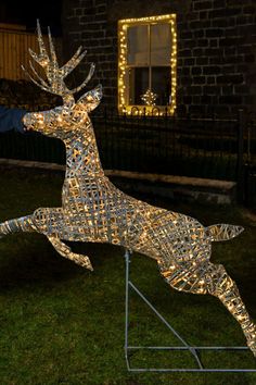 a lighted deer statue sitting on top of a metal stand in front of a brick building