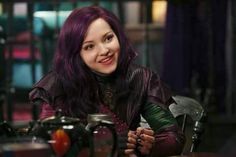 a woman with purple hair sitting at a table in front of a coffee pot and mug