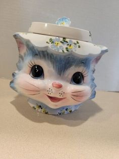 a ceramic cat cup with a hat on it's head and flowers around its neck