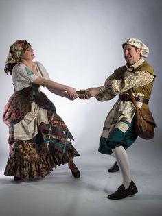 two people dressed in period clothing holding hands and dancing on a gray background with one person pulling the other's hand