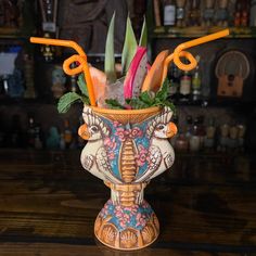 a decorative vase with orange straws and flowers in it sitting on a wooden table