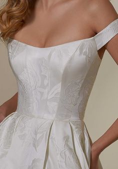 a woman wearing a wedding dress with an off the shoulder neckline