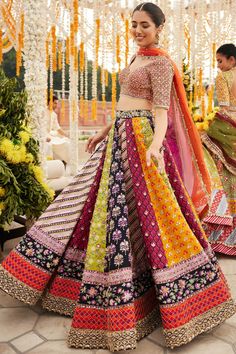 Indian Bridal Dress in Multicolored Lehenga Choli Dress is an embellished attire that will give the gorgeous bride a trendy as well as traditional bridal look. The lavish blend of colors and hand-crafted details of ornaments make this Lehenga Choli an epitome of beauty. Bridal Choli: The choli comes in an alluring blend of orange and purple shades. This stunning choli is adorned with tilla, gotta, and shimmering ornaments, making it a perfect choice to pair with the huge flared bridal lehenga, creating a flawless masterpiece for the big day. Indian Lehenga: This Bridal Lehenga has multiple colors and is emblazoned with embroidery, tilla, dabka, and gota. Beaming sequins and floral designs make this stunning Indian Lehenga an epitome of beauty and your foremost priority to have a head-turni Triple Colour Lehenga, Purple Orange Lehenga, Flower Haldi Decor, Multicolor Motif Lehenga For Wedding, Reception Sharara With Multicolor Motifs, Multicolor Motifs Lehenga For Wedding, Bohemian Traditional Wear With Motifs, Floor-length, Bohemian Floor-length Traditional Wear With Motifs, Multicolor Anarkali Set For Reception