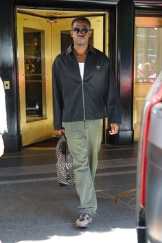 a man walking down the street carrying a handbag in his right hand and wearing sunglasses