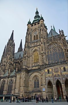 the large cathedral has many windows and spires on it's sides as well as people walking around