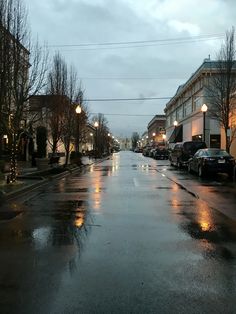 a wet street with cars parked on the side and lights hanging from the buildings at night