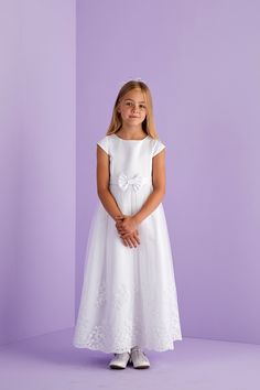 Ankle length first Holy Communion cap sleeve dress. A duchess satin dress with princess line detail, capped sleeves and front waistband with bow to centre front are complimented by the impressive scallop hem embroidery and sequin detail to the hem of the net tulle overlay skirt. Whilst at the back is a large pre tied bow with luxurious long tails completing the look and maintains a perfect bow each time you wear this dress. Fastened at the back with a hidden zip. This classic dress promotes pure Princess Style First Communion Dress With Short Sleeves, Princess Style Short Sleeve First Communion Dress, Princess Style Short Sleeve Dress For First Communion, Fitted Princess Style First Communion Dress With Short Sleeves, Princess Style Short Sleeve Dress For Confirmation, Fitted Dress With Bow For Confirmation, Short Sleeve Dress With Fitted Bodice For Confirmation, Fitted Bow Dress For First Communion, Fitted First Communion Dress With Short Sleeves