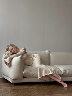 a woman laying on top of a couch with her legs crossed and arms behind her head