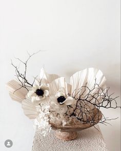 an arrangement of flowers in a vase on a white tablecloth with branches and twigs