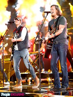 two men on stage with microphones and guitars