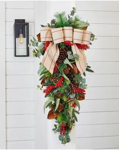 a christmas wreath hanging on the side of a white building with pine cones and evergreens