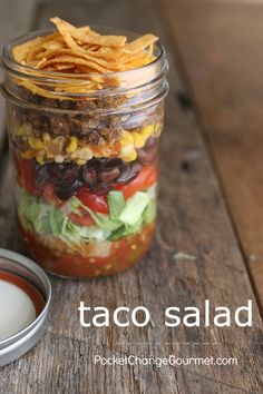 a mason jar filled with taco salad next to a container of ranch dressing on a wooden table