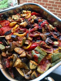 a large pan filled with lots of vegetables on top of a table next to a brick wall