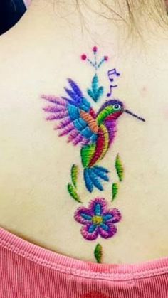 the back of a woman's neck with a hummingbird and flowers on it