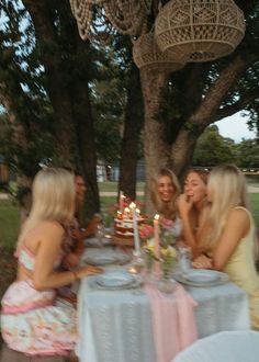 three women sitting at a table with a cake in front of them and candles on the table