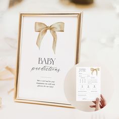 a person holding up a baby announcement card next to a photo frame with a bow on it