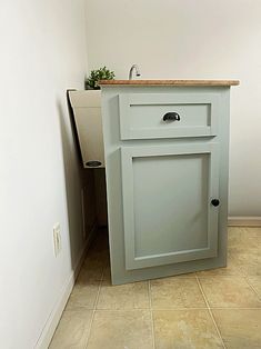 a small cabinet in the corner of a room with tile flooring and white walls