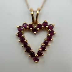 This elegant 14K yellow gold necklace features a beautiful open heart pendant adorned with vibrant red gemstone accents. The pendant measures 16.1mm x 21.4mm, making it a perfect size for everyday wear or special occasions. The heart is outlined by a series of round-cut red gemstones, each carefully set in gold prongs to create a radiant and eye-catching design.  The delicate chain measures 19" in length and is 0.6mm thick, offering a subtle complement to the bold pendant while ensuring comfortable wear. Weighing 2.09 grams, this lightweight yet durable necklace is ideal for those who appreciate fine craftsmanship and timeless beauty. The pendant's open design adds a touch of elegance, symbolizing love and warmth. 14k Yellow Gold Necklace, Red Gemstones, Delicate Chain, Open Design, Open Heart, Heart Pendant Necklace, Vibrant Red, Timeless Beauty, Heart Pendant