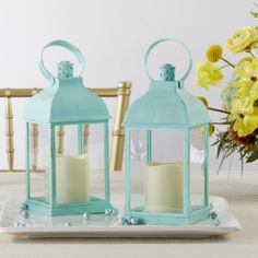 two teal colored lanterns sitting on top of a white plate next to yellow flowers