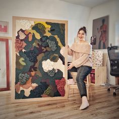 a woman sitting on a chair in front of a large piece of art that looks like flowers