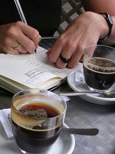 two people sitting at a table with coffee and an open book