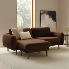 a brown couch sitting on top of a white rug in a living room next to a window