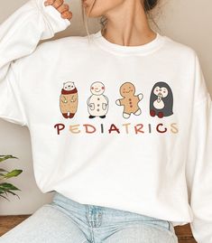 "Looking for a fun and colorful sweatshirt to wear on your Peds unit for Christmas? Look no further. This is a great gift for a pediatric nurse or healthcare worker, such as a Doctor, Nurse, Tech, or Nurse Practitioner. This unisex heavy blend crewneck is made of polyester and cotton to provide a comfortable and cozy feel. The collar is ribbed knit and retains its shape after every wash. WHAT IT SAYS:  PEDIATRICS ITEM DETAILS:  -50% cotton, 50% polyester -Medium-heavy fabric  -Loose fit -Sewn-in Playful White Sweater With Graphic Print, Cute White Christmas Sweatshirt, Novelty Cotton Crew Neck Sweatshirt, White Letter Print Sweatshirt For Gift, White Letter Print Sweatshirt As Gift, Cute Long Sleeve T-shirt As Gift, Fun White Sweatshirt For Winter, Funny White T-shirt For Winter, White Sweatshirt With Funny Print