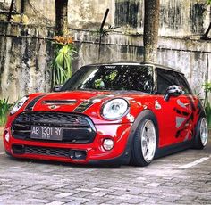 a red and black mini car parked in front of a stone wall with palm trees