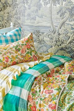 a bed covered in lots of colorful pillows next to a wall with trees and flowers on it