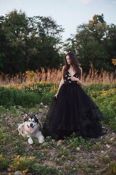 a woman in a black dress standing next to a dog