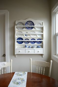 a wooden table topped with blue and white plates next to a wall mounted china cabinet