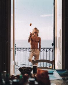 a shirtless man standing in front of an open door and throwing a frisbee