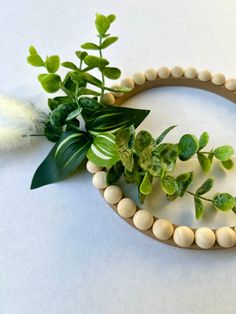 a wooden beaded bracelet with green leaves and white beads on the end, sitting next to a plant