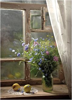 a vase filled with purple flowers next to two lemons and a window sill