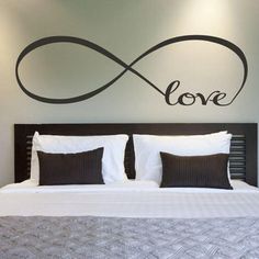 a bedroom with a large bed and love wall decal on the wall above it