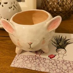 a white bunny mug sitting on top of a wooden table next to a planter