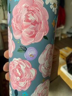 a hand holding up a blue and pink flowered cup with flowers painted on it