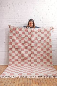 a woman is holding up a checkered blanket on a wooden floor in front of a white brick wall