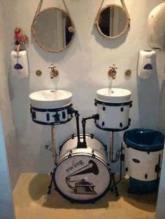 a bathroom with two sinks and three drums in front of the sink is a doll