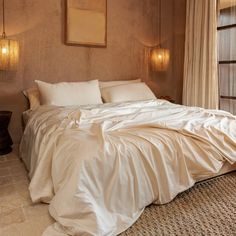 a bed with white sheets and pillows in a bedroom next to two lamps on the wall