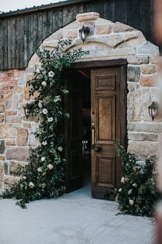 an entrance to a stone building with flowers growing on the door and brick wall behind it