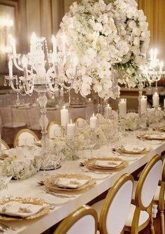 a long table is set with white flowers and gold place settings for an elegant dinner