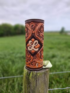 a wooden post with a brown and white leather case on it's end in front of a grassy field