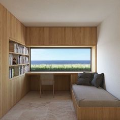 a room with a couch, bookshelf and large window overlooking the ocean is shown