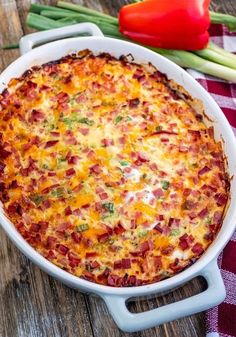 a casserole dish with cheese and vegetables on a table next to a red pepper