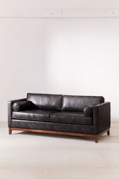 a black leather couch sitting on top of a hard wood floored floor next to a white wall